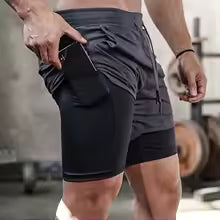 Man staat schuin en plaatst gsm in broekzak die gemaakt is voor hardlopen.